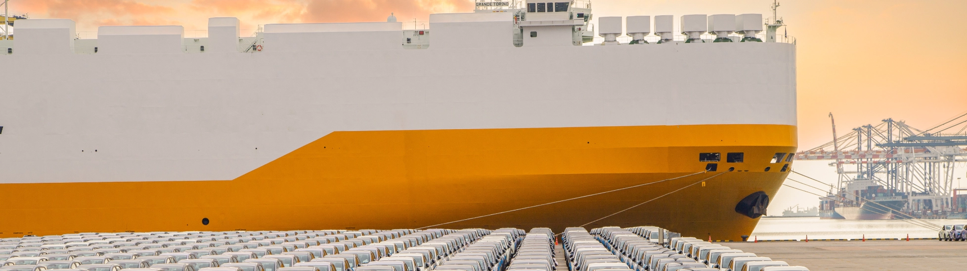 new cars parked in front of a ship in the harbour