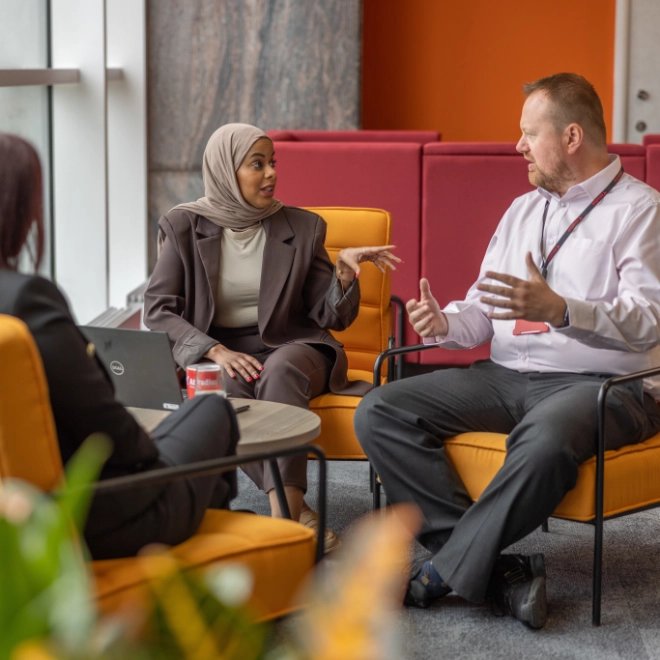 Two women and man on orange seats meeting